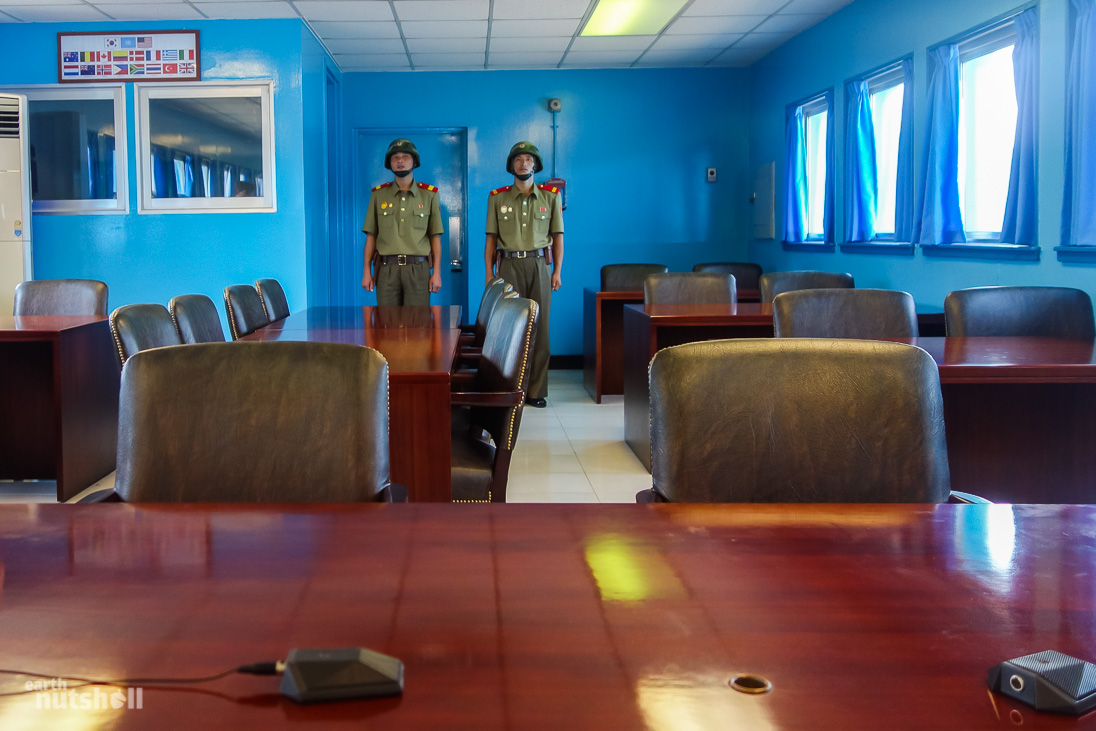 Conference room, seated at the negotiation table, facing the door to South Korea - guarded by two KPA soldiers.